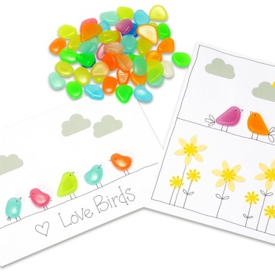 Folhas com desenho de pássaros coloridos e flores feitas com pedras coloridas sobre papel branco