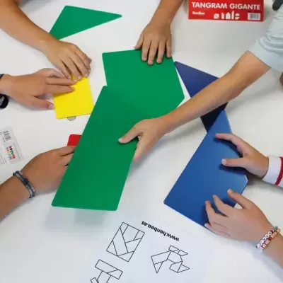 Crianças a jogar com tangram gigante colorido sobre mesa branca