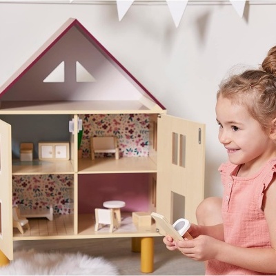 Casa de bonecas em madeira com móveis e criança sorridente ao lado