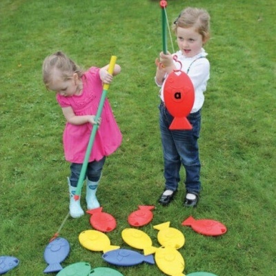Crianças a jogar jogo de pesca magnético em relvado verde com varas coloridas e peixinhos de plástico