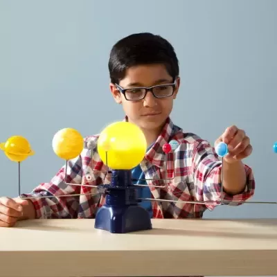 Criança mexendo em modelo colorido do sistema solar sobre mesa clara.