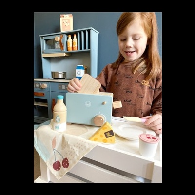 Criança a brincar com cozinha de brinquedo de madeira azul e acessórios de comida de brinquedo.