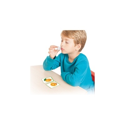 Criança a segurar pequena garrafa branca junto à boca, cartas com frutas na mesa