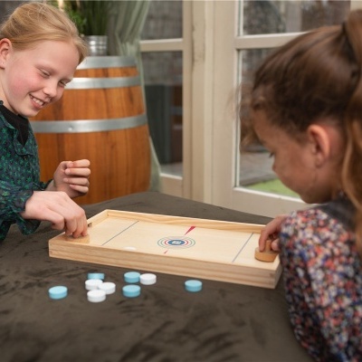 Duas meninas jogam jogo de mesa em madeira clara com peças redondas brancas e azuis