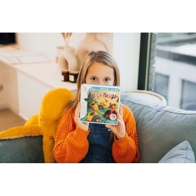 Criança segurando livro infantil Logi Bugs num sofá com almofadas