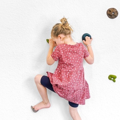 Criança a escalar parede interior com presas coloridas.