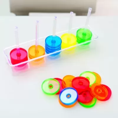 Discos plásticos coloridos empilhados e soltos num suporte e superfície branca