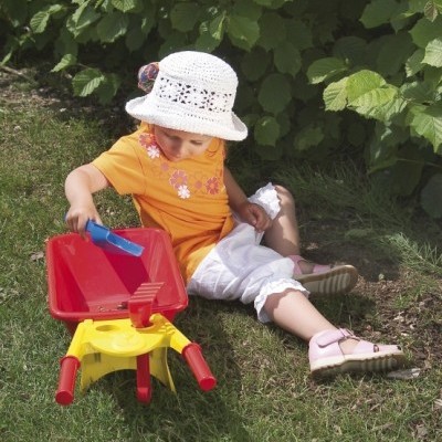 Criança com chapéu branco brincando com carrinho de brinquedo amarelo e vermelho na relva