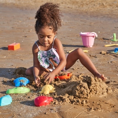 Criança a brincar na areia com brinquedos coloridos numa praia