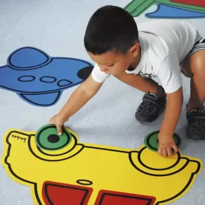 Criança a jogar peças coloridas em forma de carro amarelo e avião azul no chão.