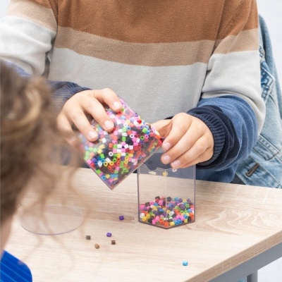 Criança a verter cubos coloridos para um recipiente transparente numa mesa