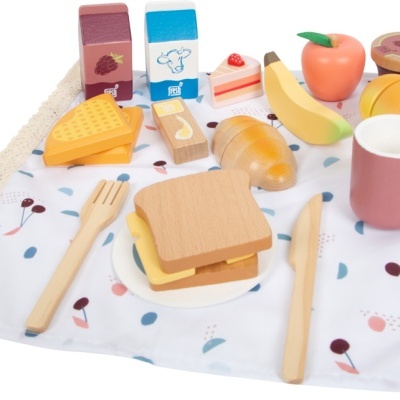Brinquedo em madeira simulando pequeno-almoço com frutas, pão, queijo, utensílios e toalha estampada.