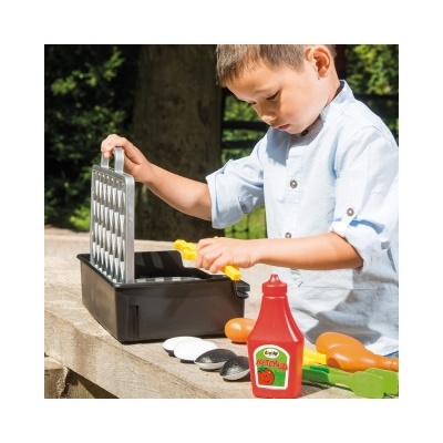Criança a brincar com brinquedo de grelhador e acessórios de comida em plástico colorido ao ar livre