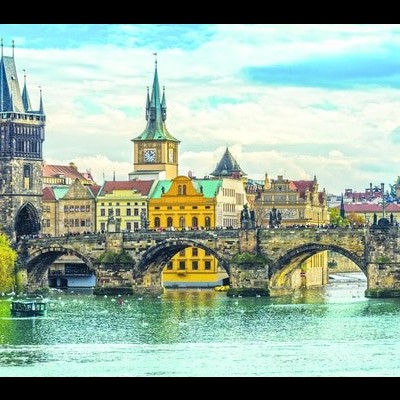 Ponte histórica de pedra sobre rio com edifícios coloridos e torres ao fundo