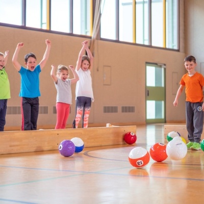 Crianças a brincar com bolas de futebol coloridas numeradas em ginásio com piso de madeira