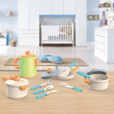 Conjunto de utensílios de cozinha de brinquedo coloridos sobre superfície de madeira com berço ao fundo