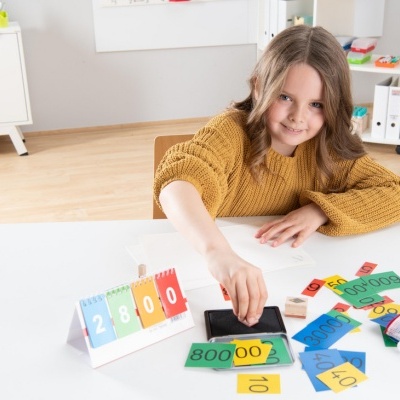 Criança a usar carimbo preto com cartões coloridos numerados em mesa branca