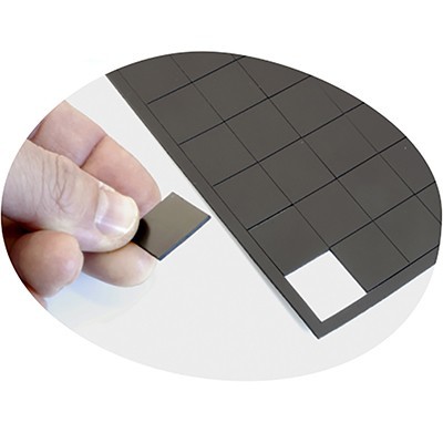 Peça quadrada preta a ser segurada sobre tabuleiro cinzento com grelha quadriculada.