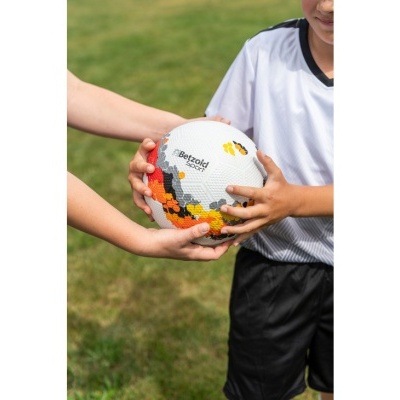 Bola de futebol colorida nas mãos de crianças num campo de relvado