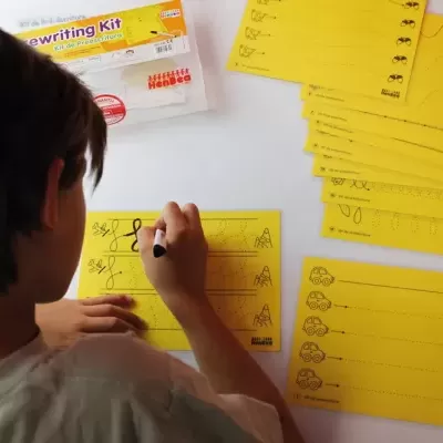 Criança a escrever em cartões amarelos de caligrafia numa mesa branca