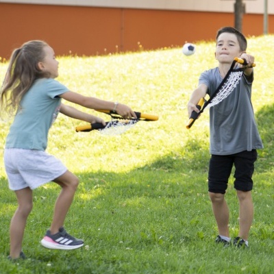 Duas crianças a jogar com redes e bola num campo verde