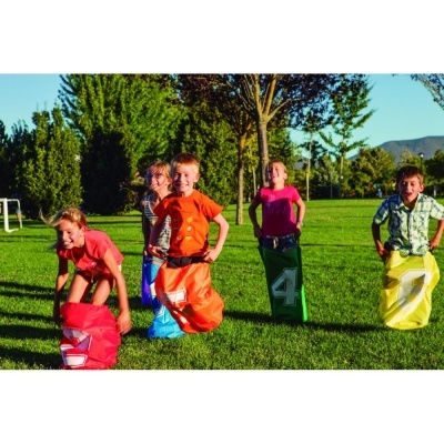 Quatro crianças a correr em sacos de pano coloridos num campo verde ao ar livre