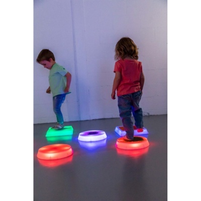 Crianças a pisar blocos iluminados de cores verde, azul e vermelho em chão cinzento