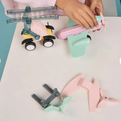 Brinquedos de avião e helicóptero em plástico colorido com rodas e hélices numa mesa branca