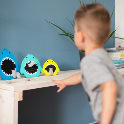 Objetos decorativos em forma de tubarão sobre prateleira branca com menino e planta ao fundo