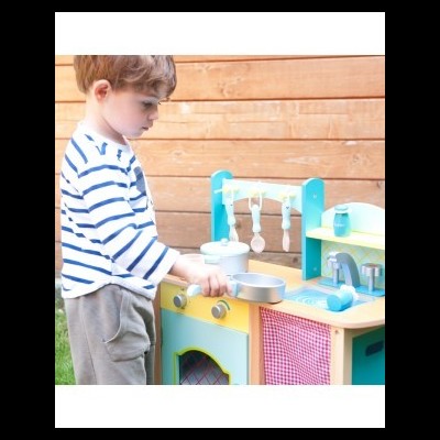Menino a brincar numa cozinha de brinquedo em madeira colorida