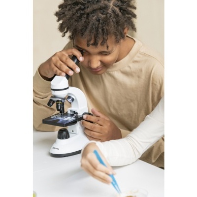 Menino a olhar para microscópio branco numa mesa branca