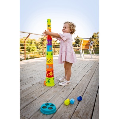 Criança a brincar com brinquedo empilhável colorido num ambiente exterior com madeira e cadeiras.