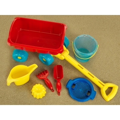 Brinquedos de praia coloridos em plástico sobre areia, com carrinho, balde, concha, ancinho, pá, forma e peneira.