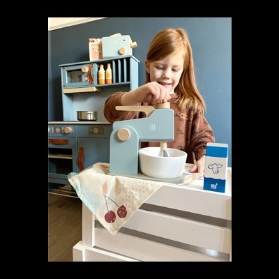Menina a brincar com batedeira de brinquedo numa cozinha de brinquedo azul
