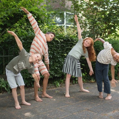 Quatro crianças descalças a fazer alongamentos ao ar livre numa calçada