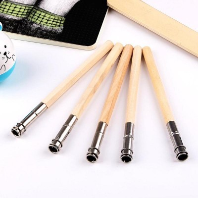 Cinco canetas de madeira com ponteiras metálicas sobre fundo branco, perto de livro, bola decorada e régua de madeira.