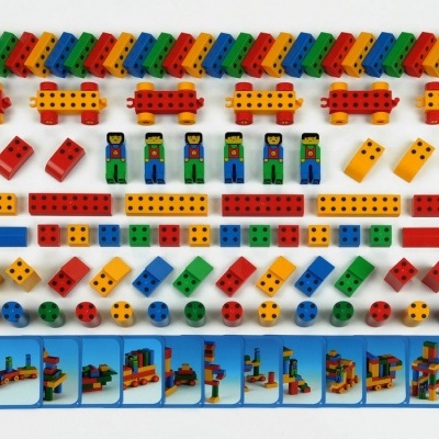 Peças de construção coloridas com figuras humanas e rodas, e guia de instruções na parte inferior.