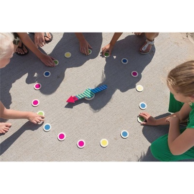 Jogo de tabuleiro com peças coloridas e uma seta de madeira numa superfície cinzenta ao ar livre