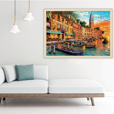 Quadro decorativo colorido de paisagem de canal sobre sofá branco com almofada azul numa sala com parede branca e candeeiros pendentes.
