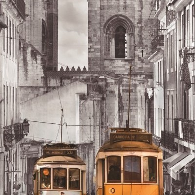 Dois elétricos amarelos numa rua antiga com edifícios e grande estrutura de pedra ao fundo