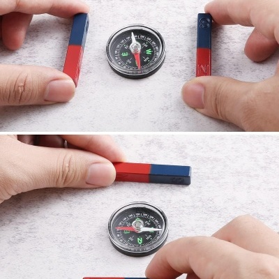 Duas mãos segurando ímanes bicolores e bússola num fundo cinzento.