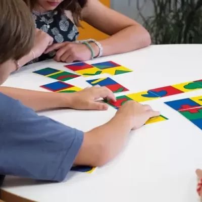 Crianças jogando jogo de cartas com formas e cores variadas num ambiente interno.