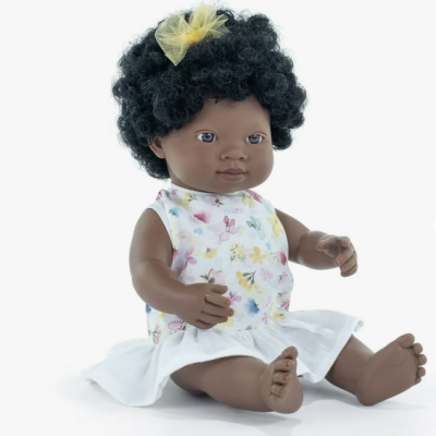 Boneca bebé de cabelo encaracolado com vestido floral sentada.