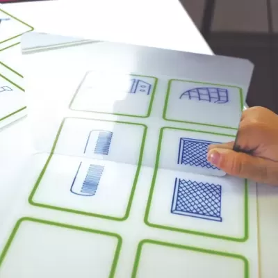 Mão a virar carta de jogo com padrões geométricos azuis em cartas com moldura verde sobre mesa branca