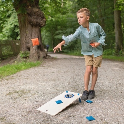 Criança a jogar cornhole num parque com tábua branca e sacos azuis