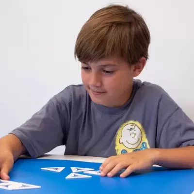 Menino com t-shirt cinzenta a brincar com peças triangulares na mesa azul
