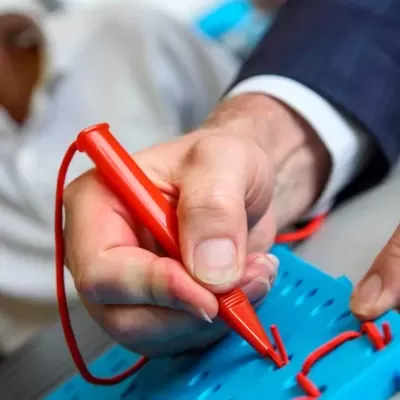 Mão a segurar uma caneta vermelha em cima de base azul com fios vermelhos