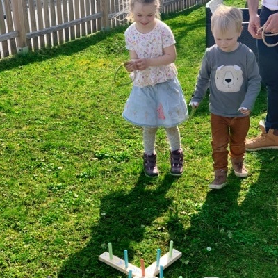 Jogo de argolas com base de madeira e pinos coloridos no relvado com duas crianças a jogar