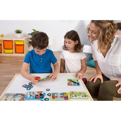 Crianças a jogar jogo de tabuleiro colorido numa mesa branca com mulher a observa-las num quarto interior