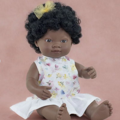 Boneca com vestido branco floral e cabelo encaracolado com laço amarelo sentada sobre fundo rosa